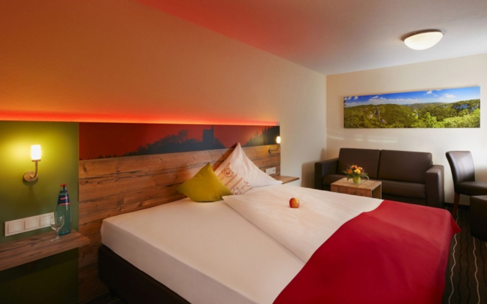 Themed image of a hotel bed in a modern room with brown leather couch and red backlighting on the bed