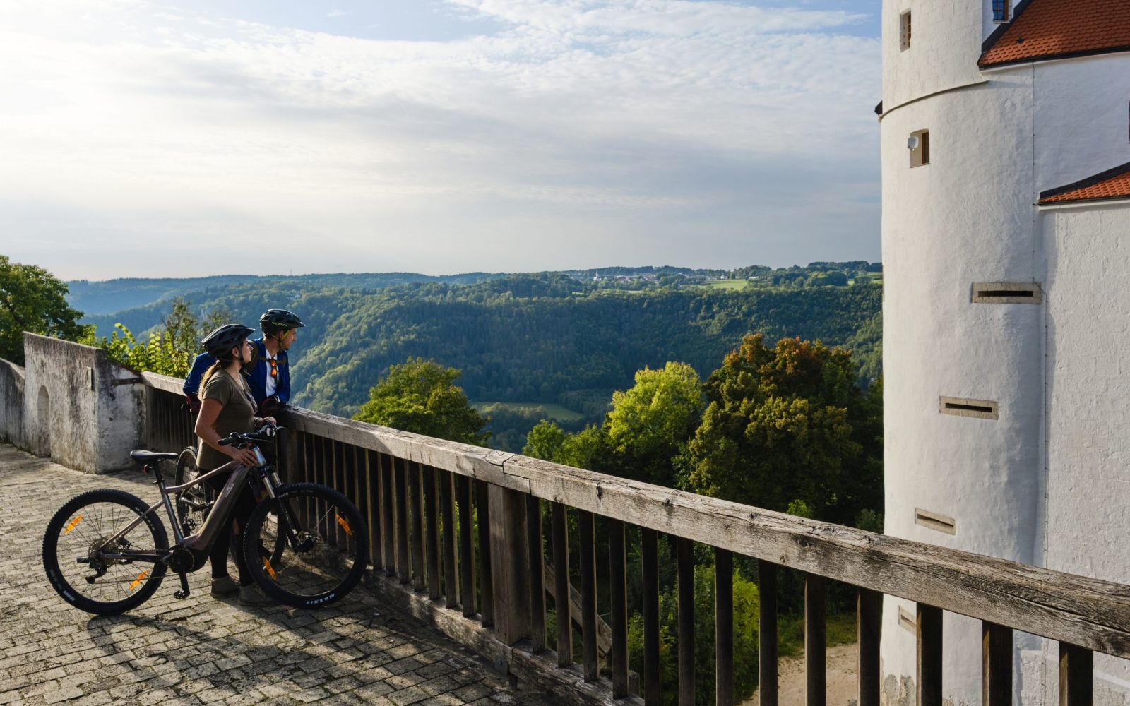 Themed picture with two cyclists looking out into nature from the railings in front of Wildenstein Castle