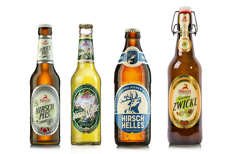 Bild von vier verschiedenen Bierflaschen der Hirsch Brauerei. Hirsch Pils, Donau Radler, Hirsch Helles und naturtrübes Zwickel in der Bügelflasche