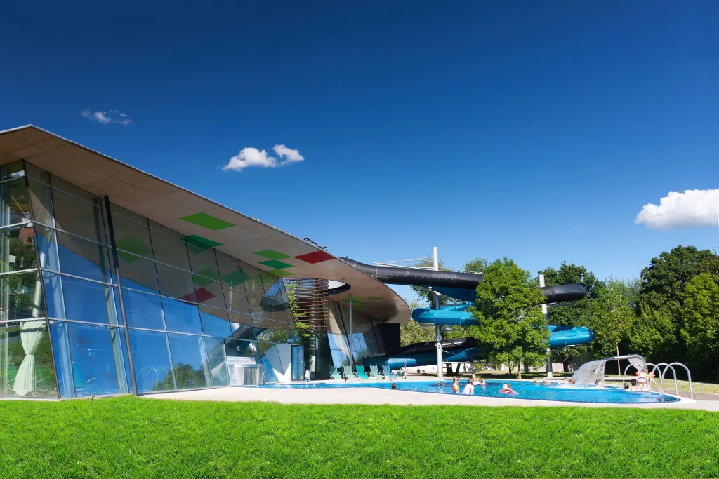 Picture of the slide landscape and the current channel in the outdoor pool in Tuttlingen with trees in the background and a blue sky with a few fleecy clouds