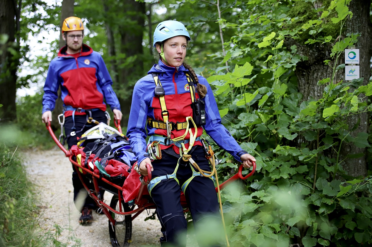 Bild von zwei Personen der Bergwacht im Einsatz mit einem Wagen zwischen sich als Trage