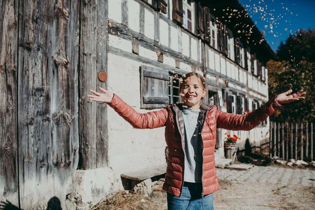 Picture of a child in front of a half-timbered building in the Neuhausen ob Eck open-air museum, letting the chaff fly over him