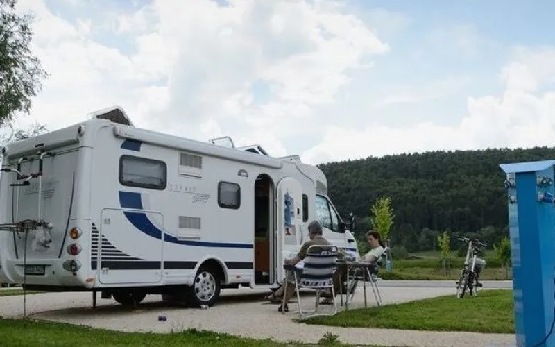 Picture of a camper on the motorhome site in Geisingen. Two people sit next to your camper and read. The sky is cloudy