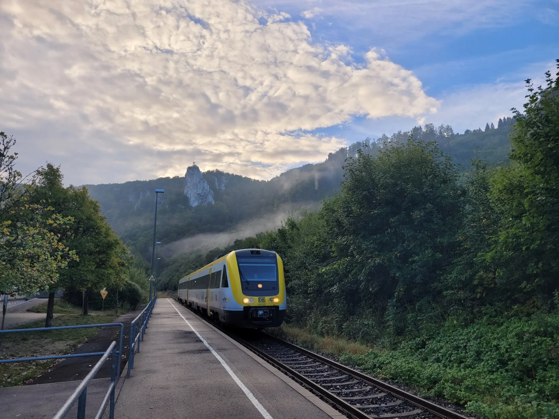 Picture of a train arriving at Beuron on the railroad track. A rock with a cross can be seen in the background