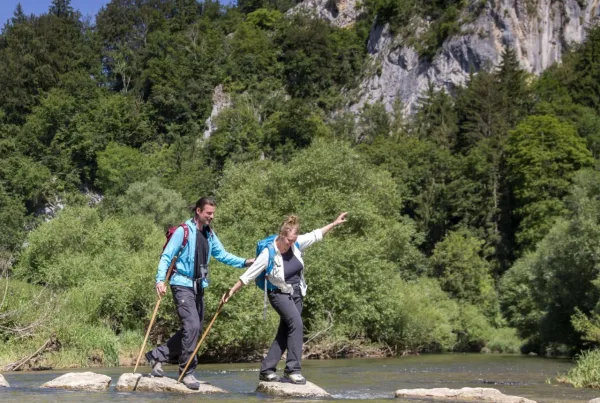 Ein Mann und eine Frau balancieren auf Trittsteinen durch die Donau