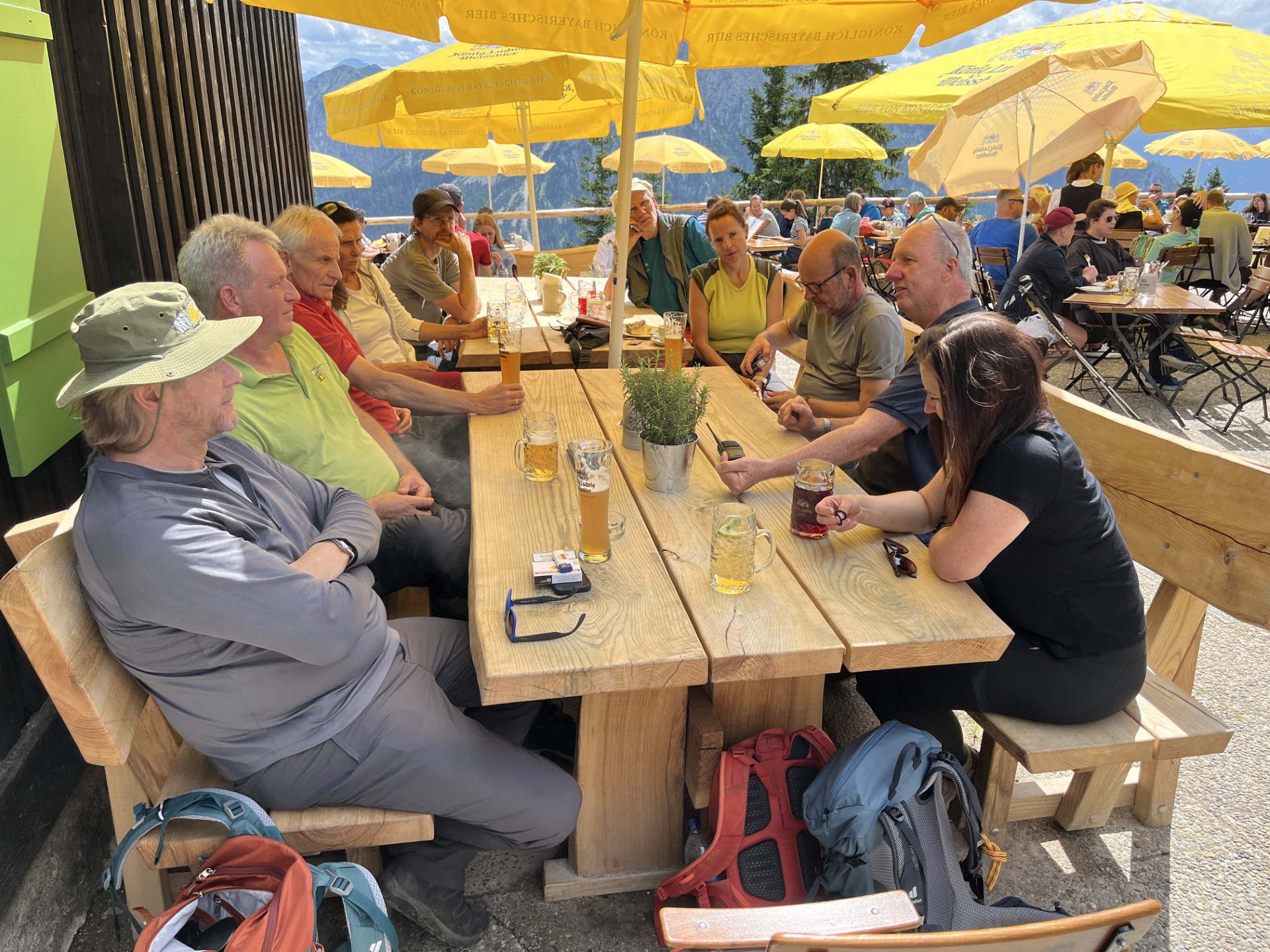 Menschn auf Ausflusgterrasse mit Holztischen und Bänken und gelben Sonnenschirmen im Gespräch bei Tagung